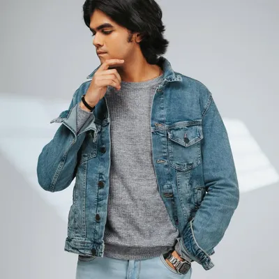 A classic men's fashion shot, featuring a denim jacket layered over a sweater. The thoughtful pose and clean lighting make this perfect for a brand's lookbook or catalog.