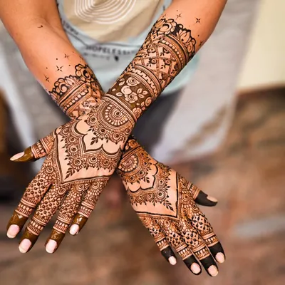A classic and dense bridal mehendi design. The palms are covered in a symmetrical pattern featuring a central heart-shaped motif, surrounded by detailed floral and geometric work that extends up the forearm.