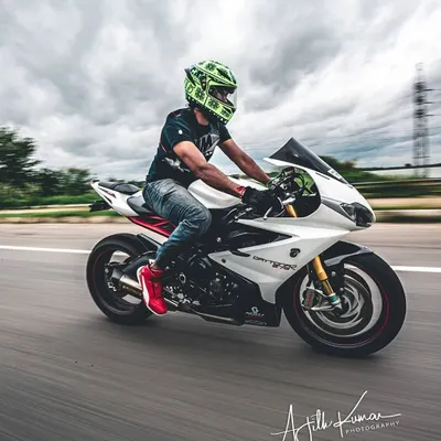 A crisp panning shot of a white Triumph Daytona motorcycle on the highway, keeping the rider sharp while the background is a blur of motion.