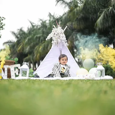 An outdoor shoot with a touch of drama. We used a yellow smoke effect to add a magical feel to this teepee setup, which includes 'ONE' letters, lanterns, and balloons.