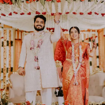 A moment of pure celebration as Yash and Jestha raise their hands in triumph after their South Indian wedding ceremony. The vibrant colors of the decor and their attire create a joyous and energetic scene.