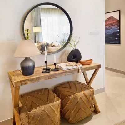 This entryway vignette in the Breeze Home proves you don't need a large foyer to make a great first impression. A slim console table, a round mirror, and pouffes that can double as extra seating create a nook that is both stylish and functional.