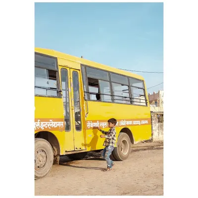A young boy reaches for the side of a yellow school bus on a dusty road in Rajasthan. This is a simple, candid moment from my travels through the state.