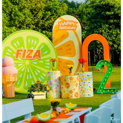 The main photo zone for a 'Two-tti Fruity' party, celebrating a second birthday. I designed oversized citrus slice backdrops, a personalized name sign, and a large light-up number '2' for a zesty and vibrant look.