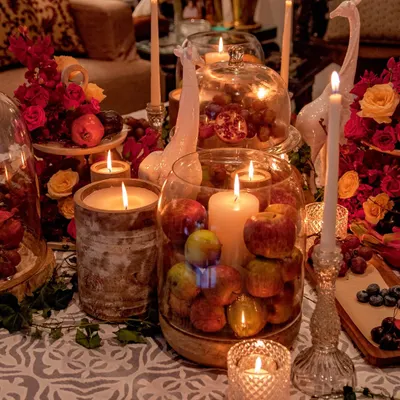 An opulent tablescape designed for an intimate wine and cheese evening. The scene is a rich tapestry of deep red florals, fresh fruits like apples and pomegranates, and an abundance of glowing candles, creating a warm and indulgent atmosphere.