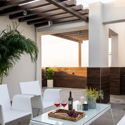 For this Jaipur penthouse terrace, we created an elegant outdoor living room. The space features a wooden pergola for partial shade, crisp white furniture for a modern look, and potted palms to add a touch of green against the city view.