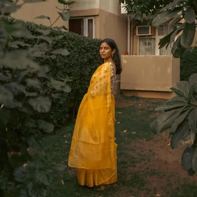 A full-length portrait of a woman in a yellow saree, framed by lush garden foliage. This composition highlights the elegance of the drape in a natural, serene environment.