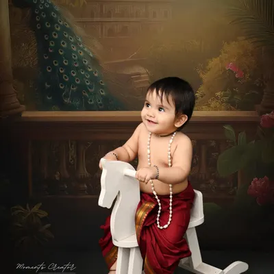 A little prince on his rocking horse. Dressed in a traditional dhoti, this baby boy looks regal and charming against a classic, painterly backdrop with a peacock.