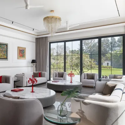 This formal living room is designed for large family gatherings, with ample seating and floor-to-ceiling windows that offer panoramic views of the garden. The neutral palette is punctuated by pops of red, creating a space that is both sophisticated and welcoming.