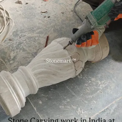 The process begins. An artisan uses a power tool to do the initial shaping of a stone pillar for a birdbath fountain. This is where the raw stone starts to take form.