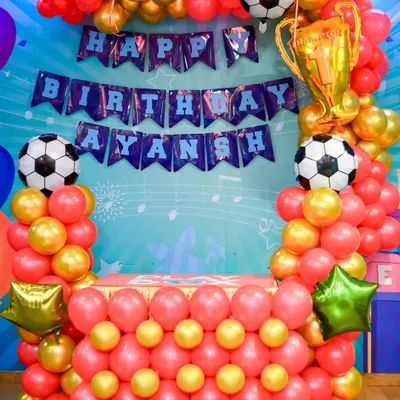 A vibrant football themed birthday setup. This includes a personalized "Happy Birthday" banner, a balloon arch in team colors, and trophy decorations.