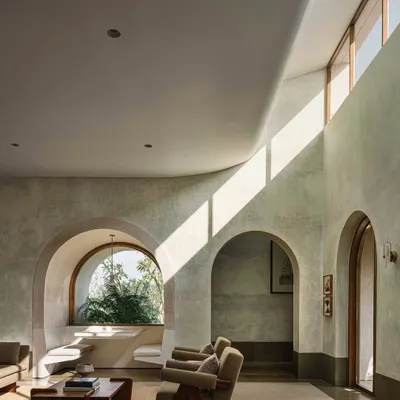 A living space at the DUA Villa, where a shaft of light from a high window illuminates the curved, lime-plastered walls. The interplay of grand volumes and intimate, carved-out niches is a hallmark of this project.