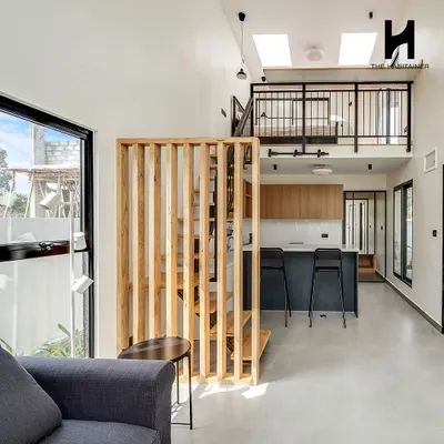 The interior of a 550 sq. ft. prefab home, showcasing a double-height living area with a mezzanine level. The open-plan design includes a modern kitchen, living space, and a staircase leading to the loft bedroom.