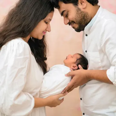 An intimate portrait of new parents with their newborn, their heads touching as they admire their baby. This pose is perfect for capturing the deep connection and love in a new family.