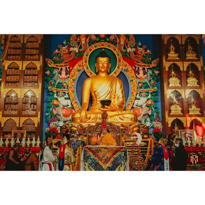 His Holiness the Dalai Lama presides over a ceremony in Bodhgaya, seated before a grand golden Buddha statue. This photograph documents a significant spiritual event, capturing the reverence and ornate detail of the setting.