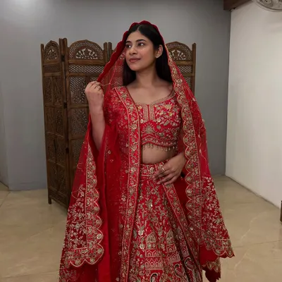 A side profile of a classic red bridal lehenga, showing the beautiful drape of the dupatta with its heavily embroidered border. This pre-loved piece is a smart choice for your big day.
