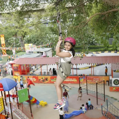 A clear, joyful shot of a child ziplining high above the park. You can see the excitement on her face as she glides through the air, fully secured in her harness.