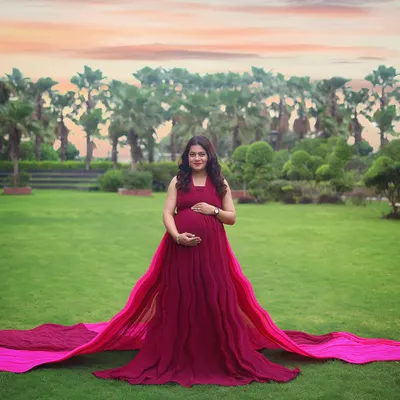 A breathtaking wide shot of the mother-to-be in a beautiful park at sunset. The long, flowing train of the gown adds a touch of drama to this outdoor maternity portrait.