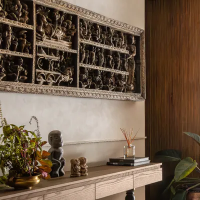 The foyer of The Collector's Retreat immediately introduces the home's narrative. A significant carved panel from the client's collection is the focal point, grounded by a simple console and warm wood paneling.