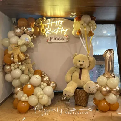 A complete view of our teddy bear themed first birthday decor, including the balloon arch with small teddy bears, a large bear prop holding balloons, and a custom number '1' balloon stand.
