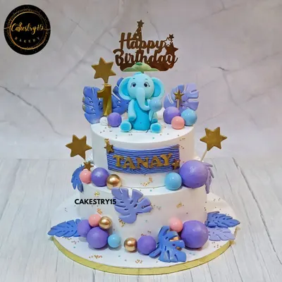 An adorable two-tier elephant-themed cake for a first birthday. This 2kg blueberry cake features a 3D fondant elephant, jungle leaves, and a dreamy blue and purple color scheme.