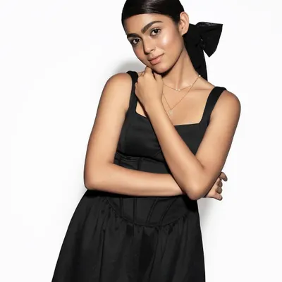 A chic and modern look featuring a sleek ponytail with a large bow accessory. The makeup is dewy with a nude lip, perfect for brown skin tones.
