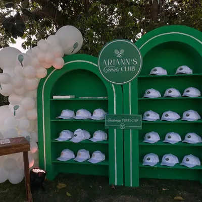 For a first birthday, I created "Arjann's Tennis Club," featuring this custom-built display wall. It held personalized caps for guests, serving as both a unique decor piece and a memorable party favor.
