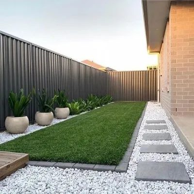 A modern and minimalist garden path created with rectangular stone pavers set in a bed of white pebbles. This design is not only visually clean but also low-maintenance and effective for drainage.
