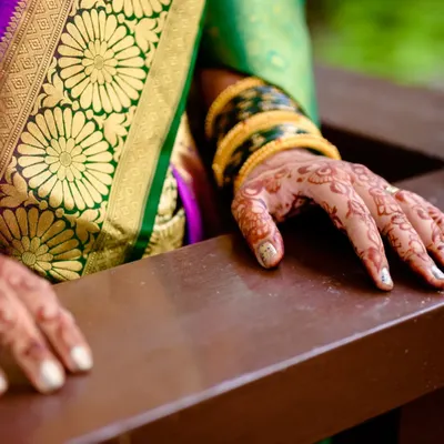 A close up of the bride's hands, showcasing her beautiful mehendi and traditional green bangles against the rich texture of her saree. These details are an essential part of the bridal look.