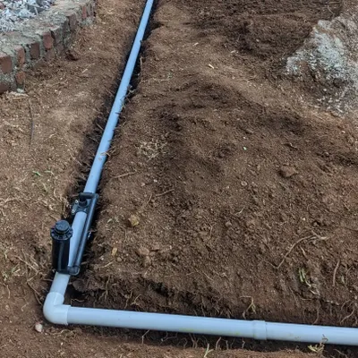 A pop-up sprinkler head is installed along the mainline pipe. This is part of an efficient irrigation system designed to provide even water coverage for a healthy lawn.