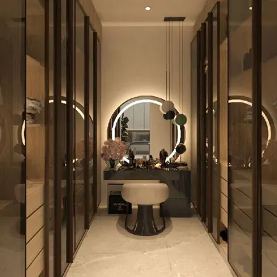 A luxurious walk-in closet featuring floor-to-ceiling glass-door wardrobes and a central vanity. The circular backlit mirror and elegant stool create a glamorous, boutique-like dressing experience.