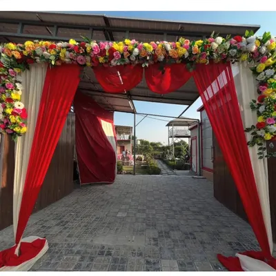 A beautiful floral archway to welcome guests to the wedding venue. The entrance is decorated with red and white drapes and topped with a border of colorful fresh flowers.