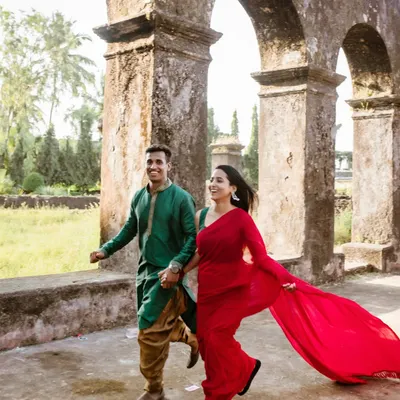 A dynamic, joyful shot of the couple running hand-in-hand through the arches of a historic fort. The bride's red saree flows beautifully, adding a pop of color and energy.