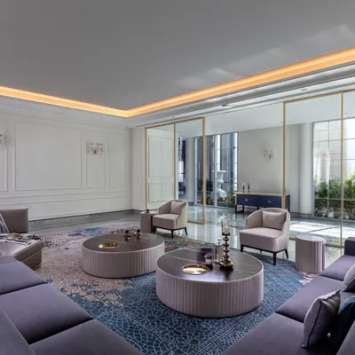 In The Grand Alabaster, soft light from the courtyard fills this formal living room, creating a warm and still atmosphere. The combination of a plush sectional sofa, a patterned rug, and classic wall paneling gives the space a sense of calm, comfort, and quiet luxury.