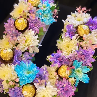 A vibrant and colorful monogram arrangement. This letter 'U' is crafted with a mix of purple, blue, and white chrysanthemums and dotted with Ferrero Rocher chocolates for an extra touch of luxury.