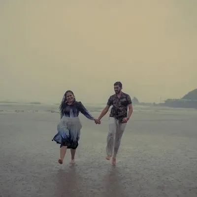 A candid moment of a couple running hand-in-hand on a rainy Goa beach. Our monsoon pre-wedding photography is all about embracing the weather and capturing the pure joy of the moment.