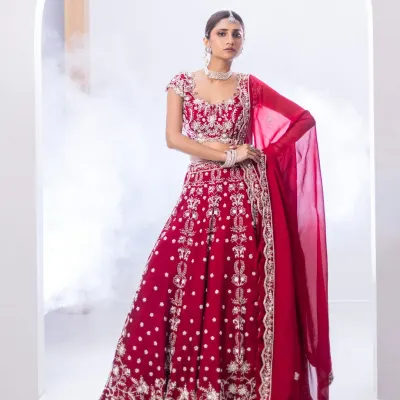 A traditional red bridal lehenga, reimagined for the modern bride. The full-volume skirt and intricately embroidered blouse, featuring sequins and metallic threadwork, create a look that is both classic and breathtaking.