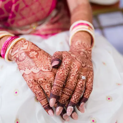 A close-up of the bride's hands, showcasing the beautiful, intricate patterns of her bridal mehndi and her engagement ring.