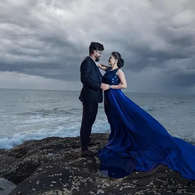 A dramatic coastal portrait with a stormy sky. The deep blue of the gown against the moody sea creates a powerful and cinematic image, perfect for couples who love a bit of drama.