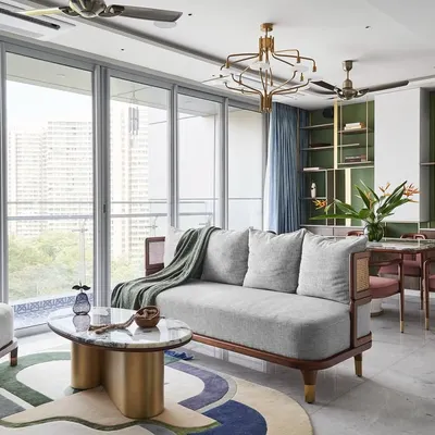 The living room of the "Whimsical House," featuring a custom 3-seater sofa and lounge chairs that blend wood and cane for a Zen-like feel. The centerpiece is the 'Ananta' table, with its infinity-shaped brass base and Patagonia marble top.