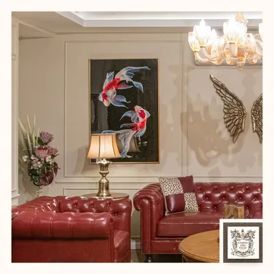The Chesterfield sofa is the epitome of timeless design. Here, in a bold red leather, it anchors the room with confidence and character, complemented by the serene koi fish art and classic gold accents.