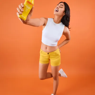 A full-length shot from the Jimmy's Cocktails campaign, capturing a moment of pure joy. The styling is bright and energetic, with the model in yellow shorts and a white crop top that perfectly matches the brand's vibrant and fun-loving identity.