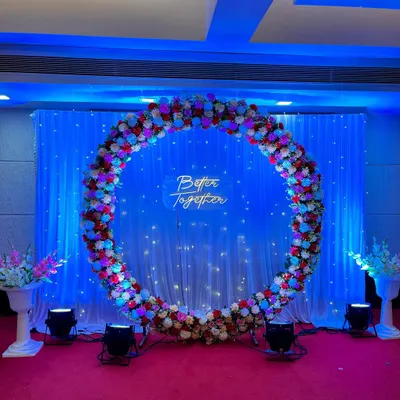 This large floral ring backdrop was designed for an engagement ceremony. The combination of red, pink, and white flowers, a 'Better Together' neon sign, and professional lighting creates a beautiful stage for the couple.