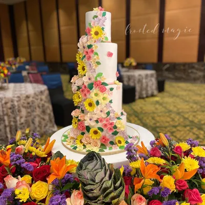 This four-tiered floral wedding cake was designed to match the vibrant flower decor of the event. It features a cascade of handmade sugar flowers, including sunflowers and cosmos, creating a stunning and cheerful centerpiece.