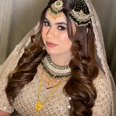 This bride's look is pure elegance. Her beige and green lehenga is paired with a soft glam makeup look, featuring voluminous curls and a perfectly placed maang tikka and passa.