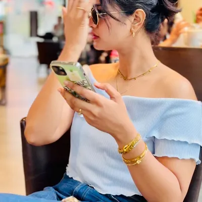 A candid-style shot capturing a model wearing delicate gold jewellery in a cafe. This lifestyle approach makes the product feel accessible and part of a desirable everyday aesthetic.