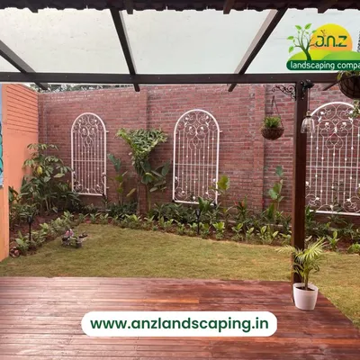 A view from the wooden deck of a villa landscape project in Kengeri. We designed this space with a natural lawn, brick wall accents, and decorative metal trellises to create a charming backyard.