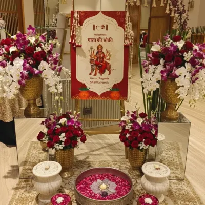 This is an elegant entrance setup for a Mata Ki Chowki. We used beautiful arrangements of red roses and white orchids in golden vases, a welcome sign with religious motifs, and traditional urlis with floating flowers.