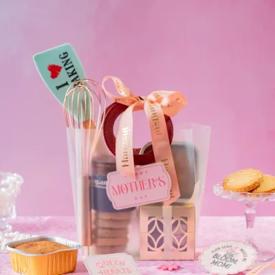 A hamper for the mom who loves to bake. This Mother's Day gift includes fun baking tools, wholesome orange cake, cookies, and calming tea, all wrapped in a chic transparent bag.