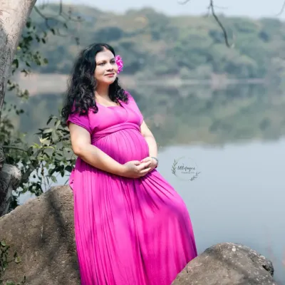A moment of quiet reflection by the water. The mom-to-be, dressed in a vibrant pink gown, looks out at the horizon, embodying the peaceful anticipation of motherhood.